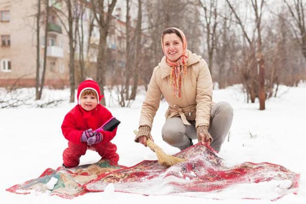 Naine ja laps puhastavad lumes vaipa