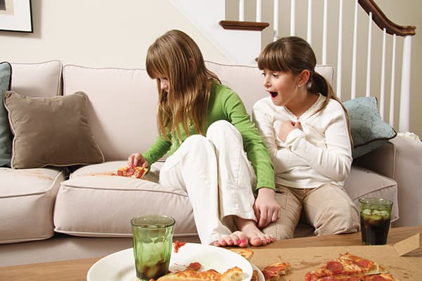 La niña dejó caer un trozo de pizza en el sofá.