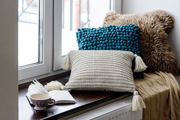 Almohadas, taza y libro en el alféizar de la ventana.