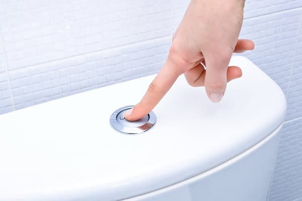 Presionando el botón de la cisterna del baño.