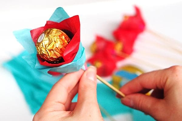Mujer hace una flor con dulces, brochetas y papel.