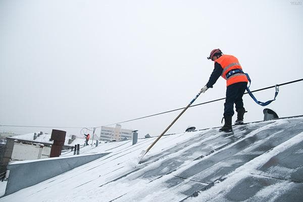 Elamu- ja kommunaaltööline puhastab õmbluskatuse lumest