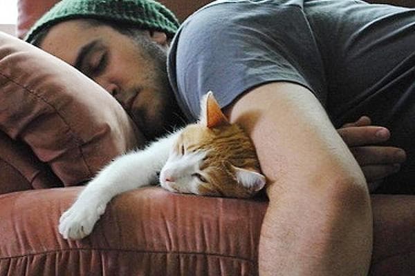 Un hombre duerme con un gato.