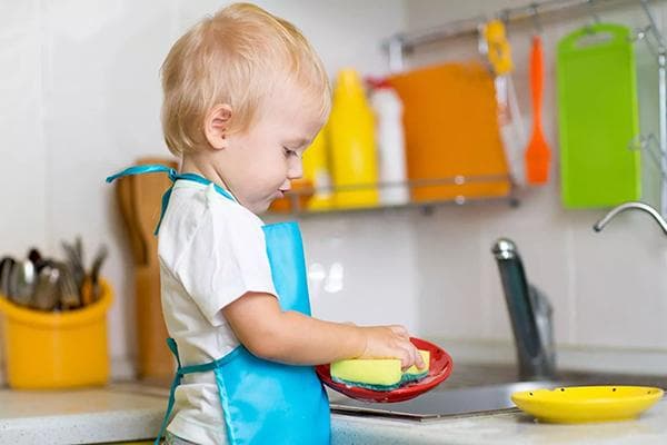 Niño en edad preescolar lavando platos