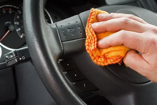 Un hombre limpia el volante de un coche con un trapo.