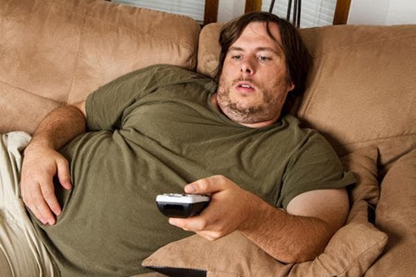 Un hombre yace en el sofá con el mando a distancia del televisor.