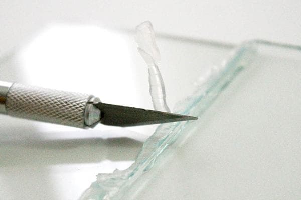 Cuchillo de papelería y restos de pegamento sobre vidrio.