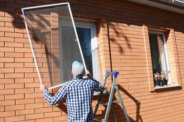 Un hombre quita un mosquitero de la ventana de una casa particular