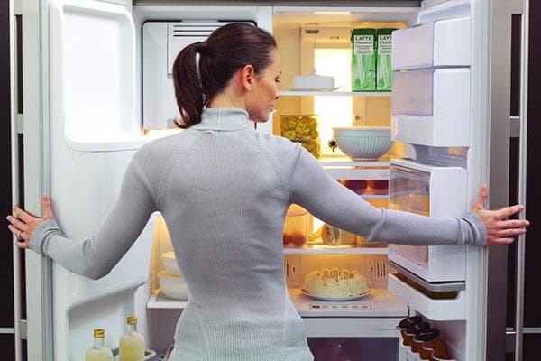 Naine toidukaupadega külmkapi juures