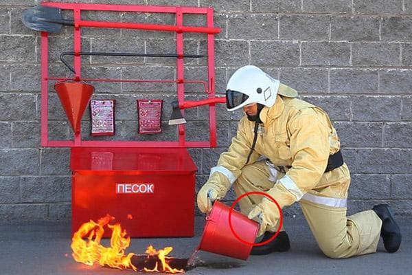 Un bombero apaga una llama con agua de un balde.
