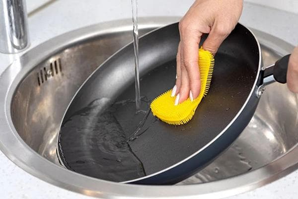Lavar una sartén con una esponja de silicona